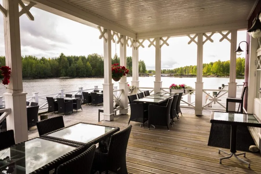 Viihtyisä terassi järven äärellä, jossa mustat muovituolit ja lasiset pöydät.