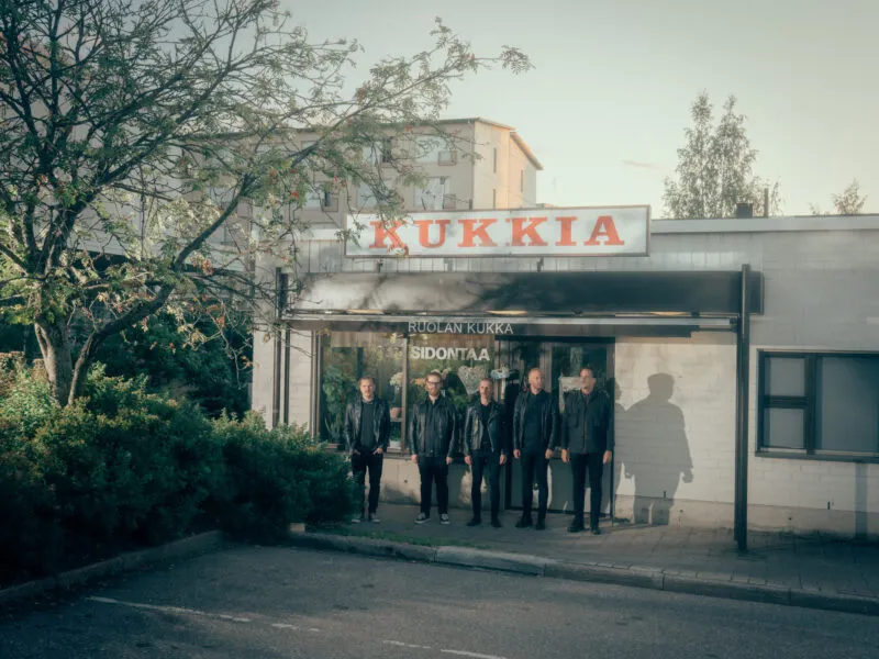 Kuusi miestä seisoo kasvitieteellisen myymälän edessä, jonka kyltti ilmoittaa "Kukkia".