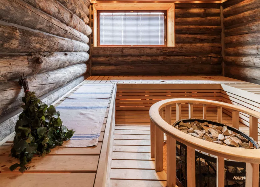 Perinteinen suomalainen sauna, jossa on puulattia, hirsiseinät, ikkuna ja kivivarasto kiukaan ympärillä.