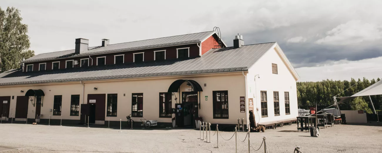 Vanha teollisuusrakennus, jossa on punaiset ikkunat ja harmaa katto, sijaitsee avaralla pihalla.