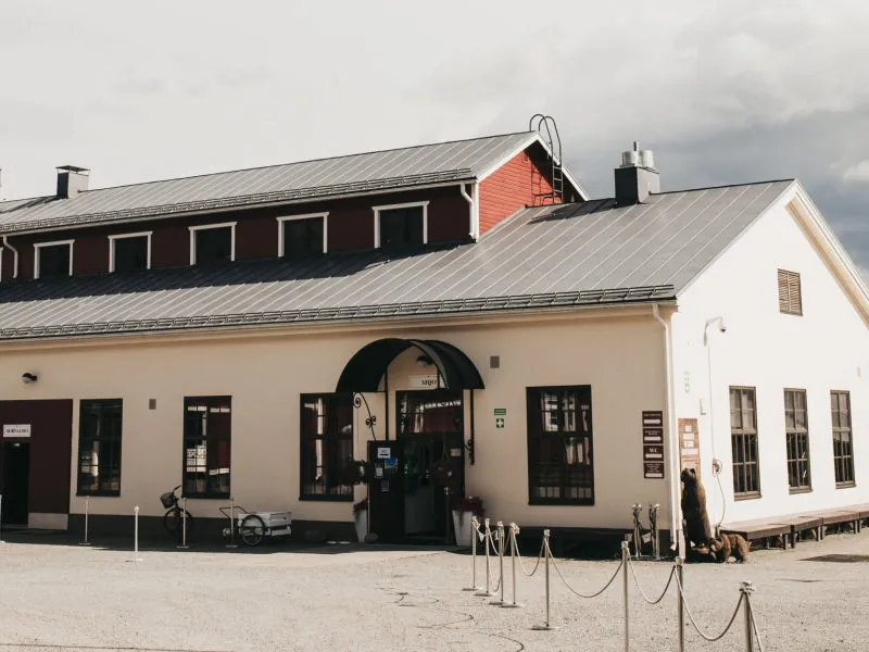 Vanha teollisuusrakennus, jossa on punaiset ikkunat ja harmaa katto, sijaitsee avaralla pihalla.