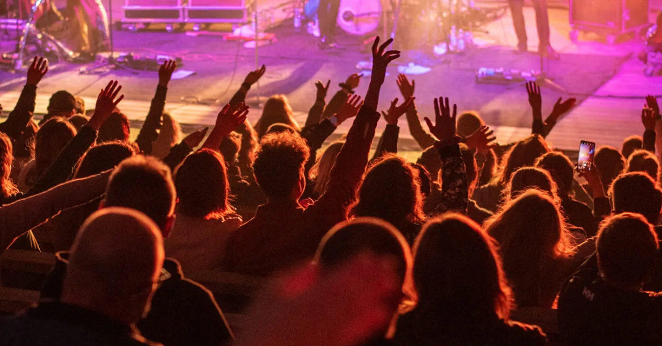 Yleisö nostaa innostuneina käsiään konserttisalissa, kun esiintyjät soittavat lavalla.