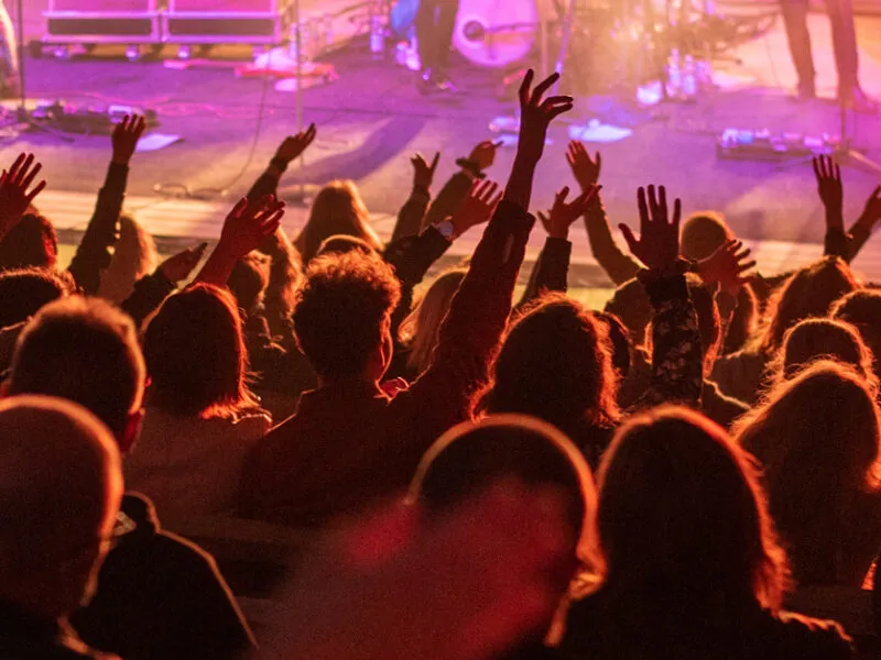 Yleisö nostaa innostuneina käsiään konserttisalissa, kun esiintyjät soittavat lavalla.