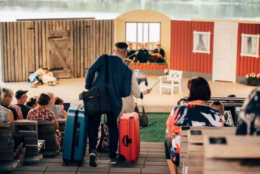 Mies kantaa värikkäitä matkalaukkuja teatterin esitystoiminnan keskellä ulkona.